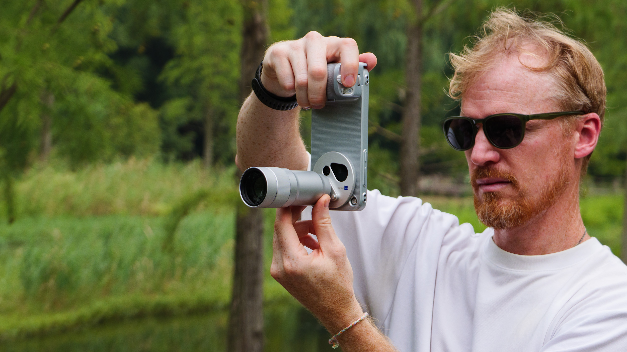 Tim Coleman, TechRadar's Cameras Editor, holding the Vivo X500 Pro Max phone with teleconverter lens attached, while stood on a wooden walkway in a birdlife reserve in Shanghai, China