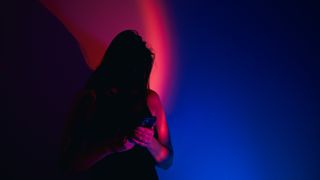 photo of a woman looking at a phone under stark red and blue light