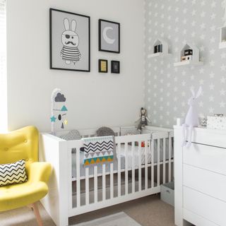 White crib, white chest of drawers, yellow armchair. four prints of wall art
