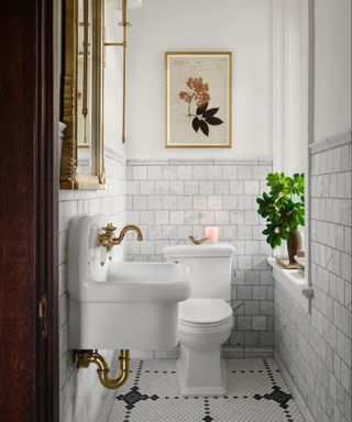 A small bathroom; a white toilet and a white sink with gold hardware and gold wat on the back wall.