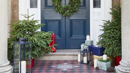 blue christmas door decorated with a wreath and surrounded by christmas trees and candles