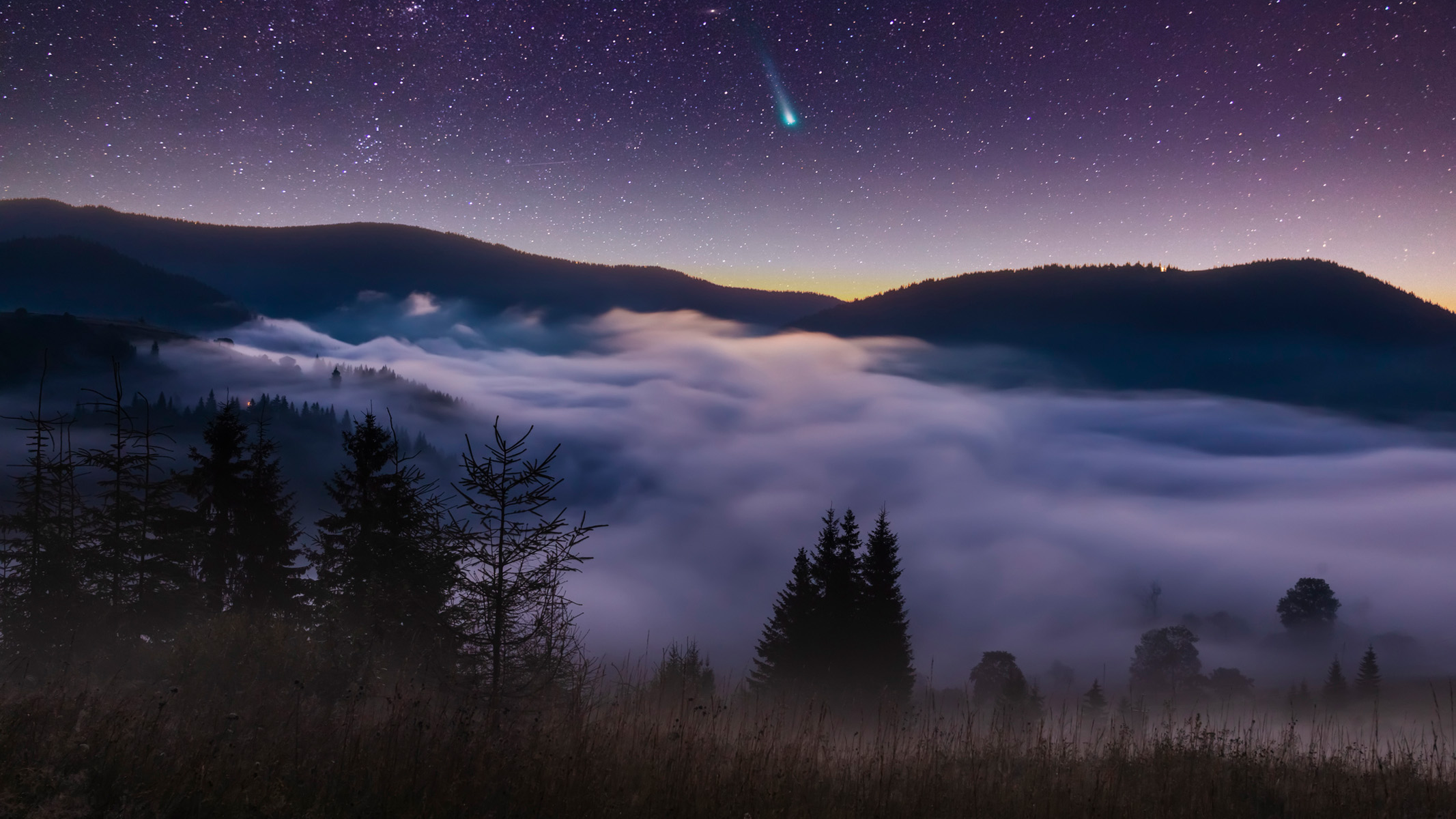 Comet C/2021 A1 Leonard at night over misty mountains