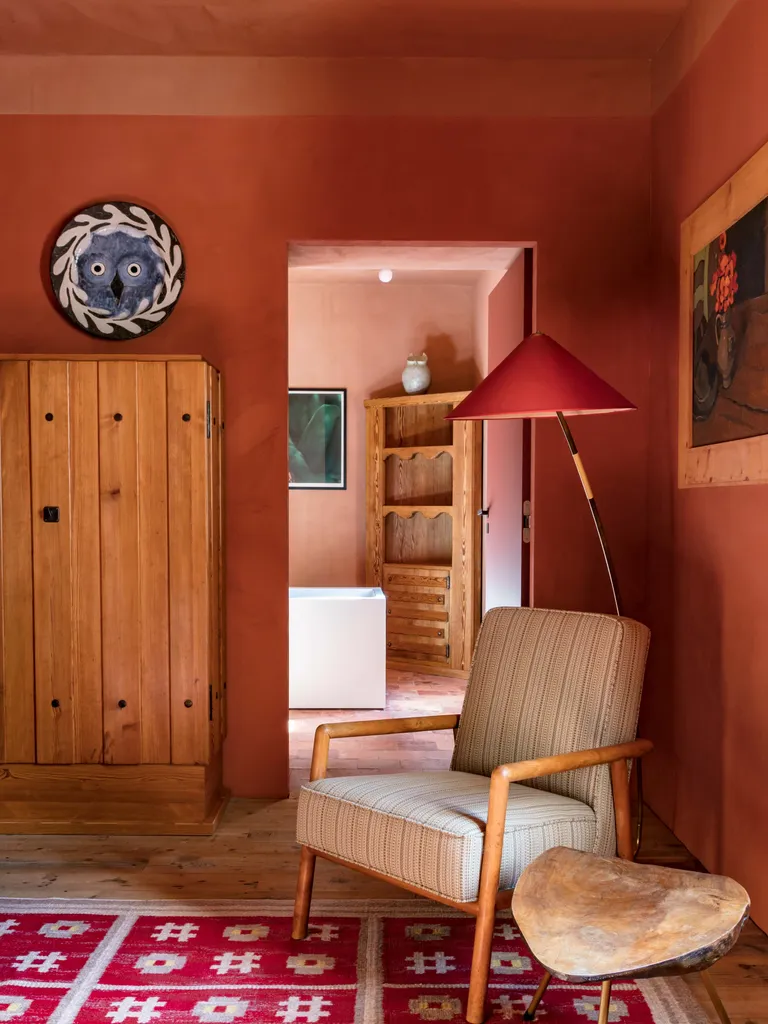 Living room with limewash-effect brick red painted walls, red patterned rug, pine furniture and neutral upholstered armchair