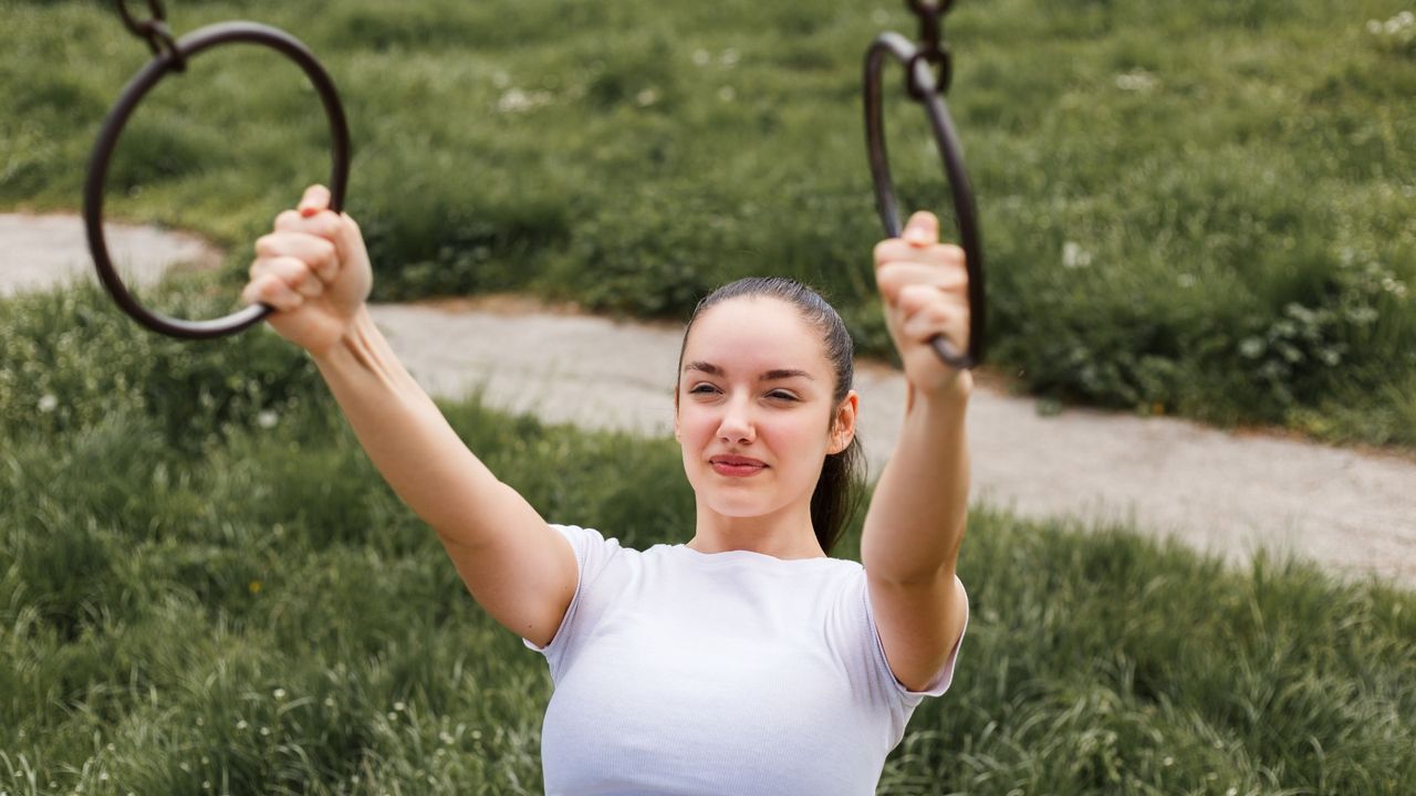 Woman outdoors rowing with her arms extended holding two gymnastic rings