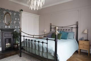 Pink bedroom with wall panelling, blue patterned feature wallpaper, black metal bed and light blue bed linen