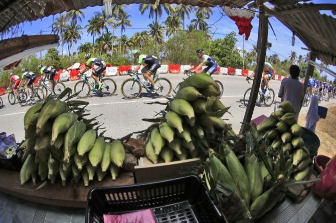 The peloton pass by a street seller