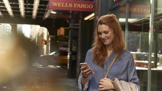 A woman looks at her phone with Wells Fargo sign in background