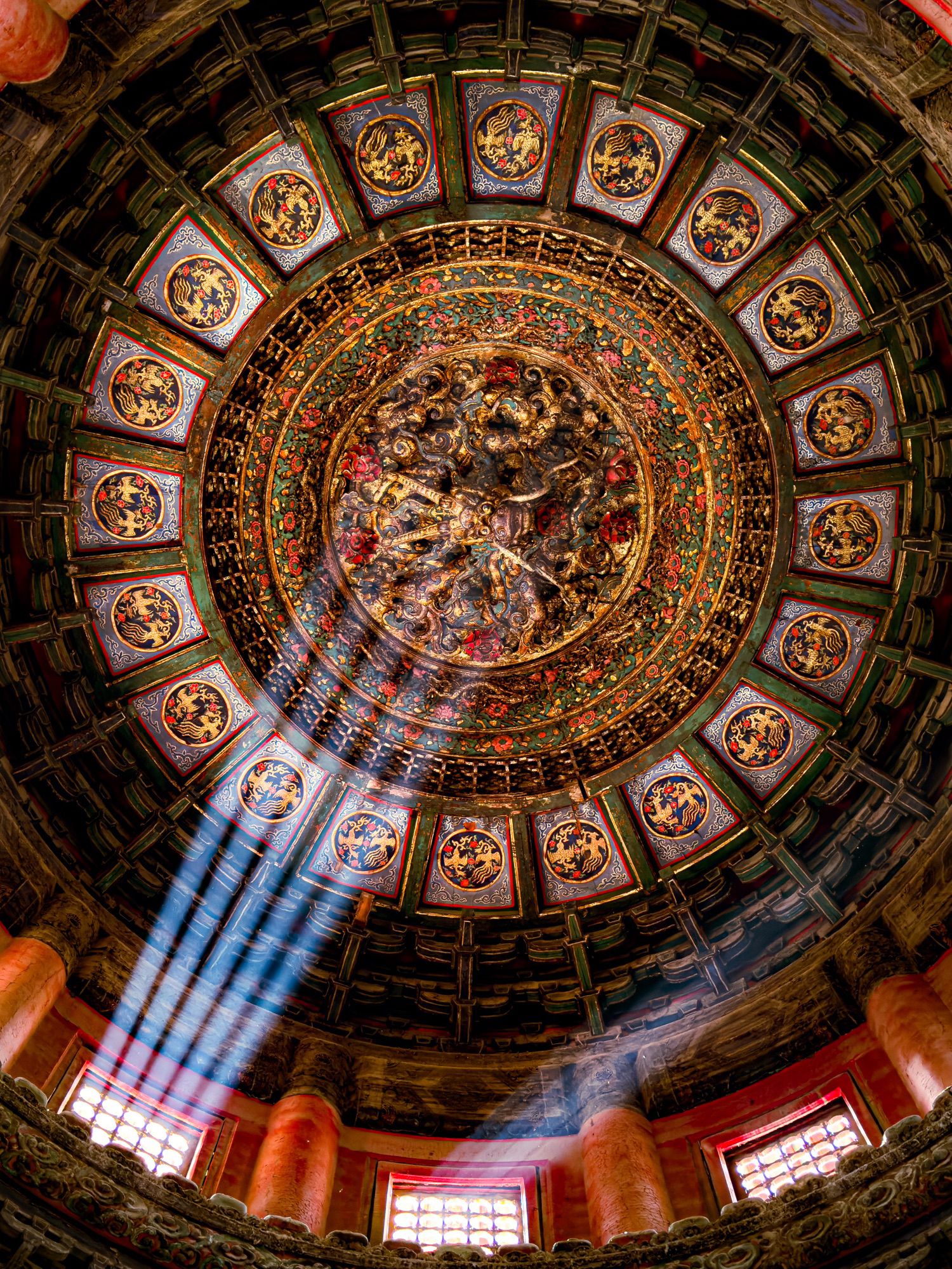 Ornate circular ceiling with intricate carvings and colorful patterns, illuminated by sunbeams through windows