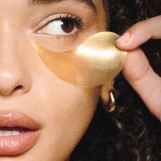 A close up of a model applying an under eye mask.