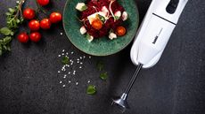 Bamix Immersion Blender on a black countertop with food to the left hand side