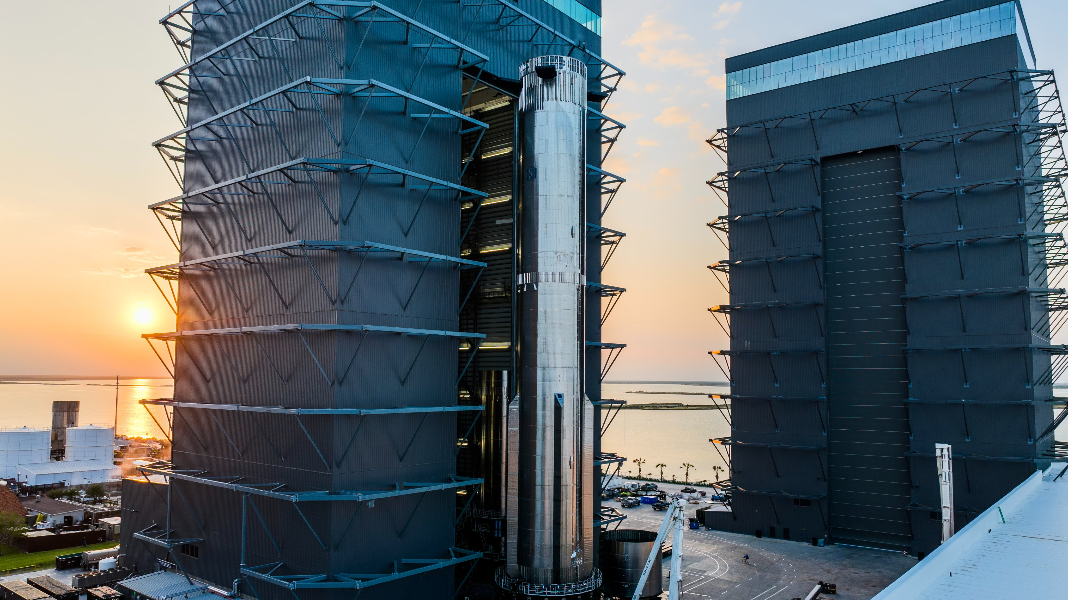 a large silver rocket exits a hangar near sunrise, with the ocean in the background