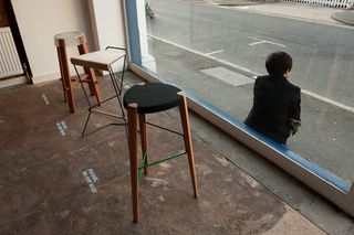 high stools on display in a store by the clear glass panel with a man sitting by the window outside the store