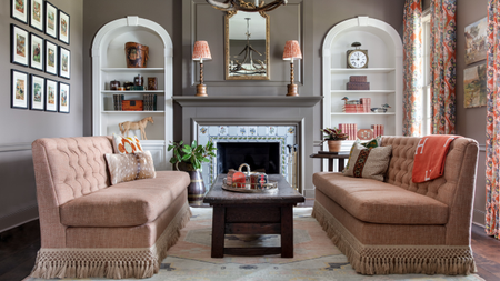 Opulent living room featuring twin fringed armless sofas flanking either side of a wooden coffee table. Elsewhere, patterned curtains, bobbin-based table lamps, and equestrian accents set the scene