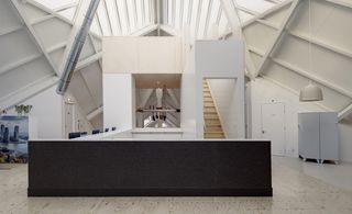 Interior view of the Super Cube featuring white, brown and wood covered walls, light coloured flooring, a pendant light, art, a light grey cupboard and wooden stairs