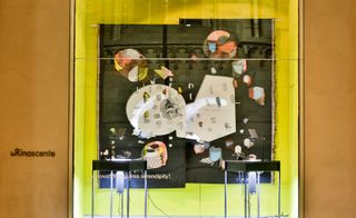 Colourful window display at the Serpentine Gallery, brown wall, yellow background art piece, black draped textiles with decorated design, two glass framed up lights
