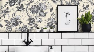 Cream and black printed bathroom wallpaper on upper half of wall with white metro tiling beneath and a decorative picture frame