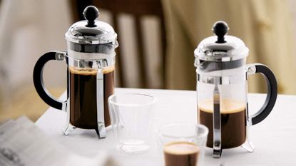 One of the best French presses, the Bodum Chambord French presses on a table with a cup of coffee in front of them