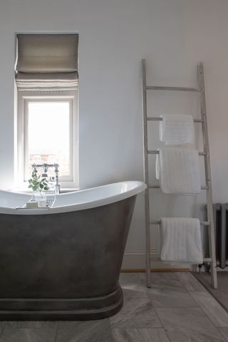 iron freestanding boat bathtub with white walls and towel ladder