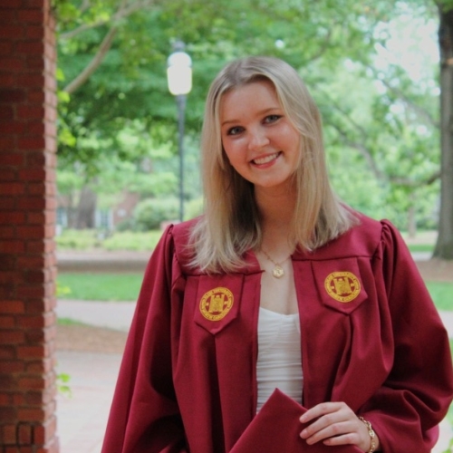 Image of a woman standing outside in a red graduation gown.