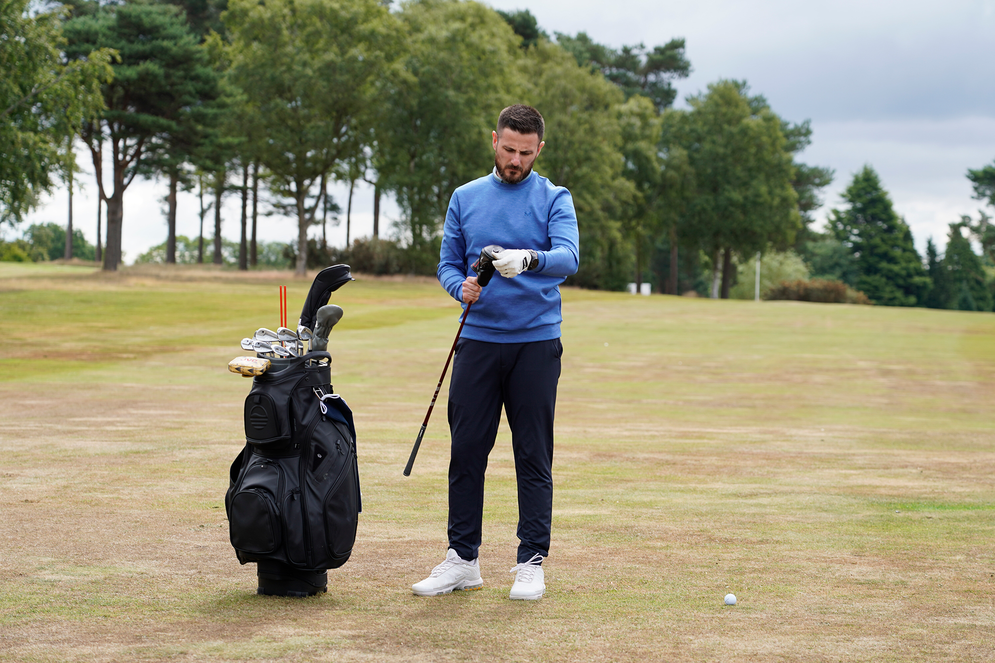 Baz Plummer pulling the head cover off his a fairway wood and looking down at the club while standing next to his golf bag