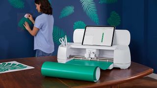 Cricut Maker vs Cricut Maker 3: The Cricut Maker 3 and roller accessory on a table with a woman