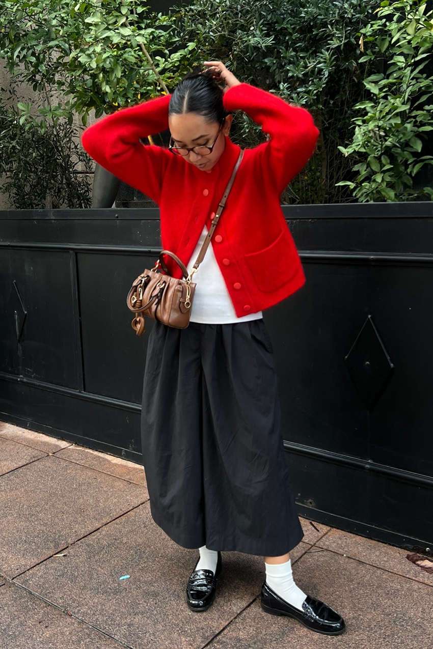 a woman wearing a red caridgan, white tee, black culottes, and black loafers