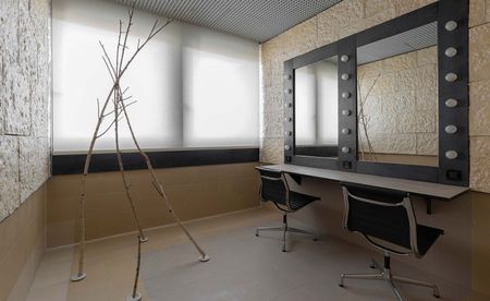 A changing room at Teatro degli Arcimboldi, Milan, featuring a composition of branches and two black chairs in front of mirrors