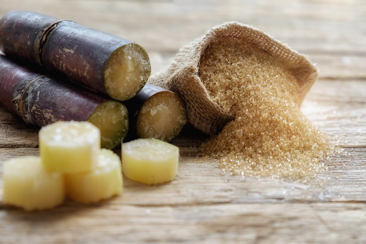 Small Bag Of Sugar Next To Cut Up Sugarcane