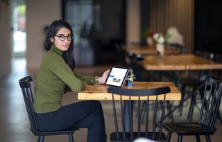 eine junge Frau sitzt in einem Cafe und nimmt an einem Onlinemeeting teil