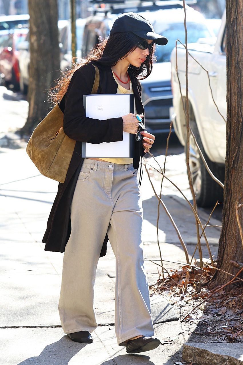 Zoë Kravitz wearing a black cardigan, baseball cap, and hat with khaki jeans in NYC.