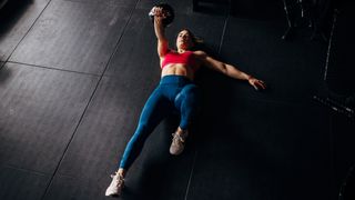 Woman in starting position of Turkish get-up exercise, lying on her back holding a kettlebell above her