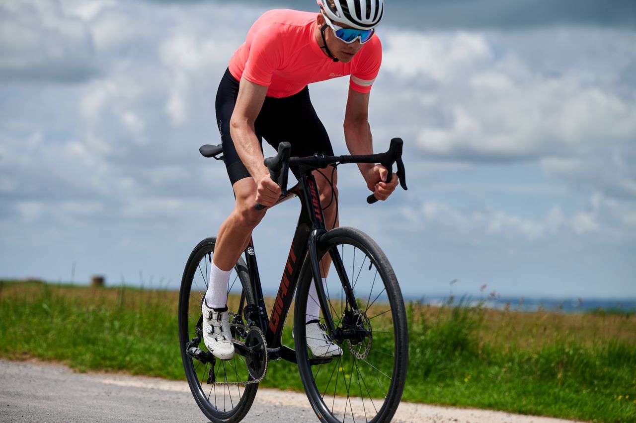 Cyclist in pink top out of saddle on Giant road bike