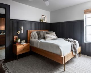 bedroom with wood paneling painted dark blue, with a wooden bed frame in the middle