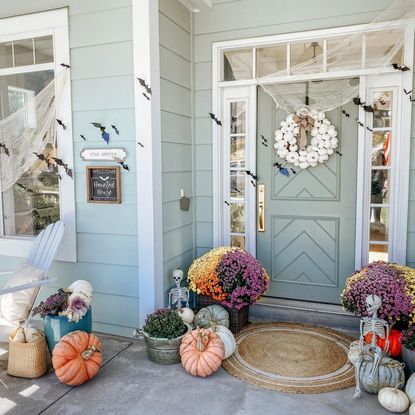 Blue painted home with Halloween decorated porch, mums and pumpkins gathered around the front door