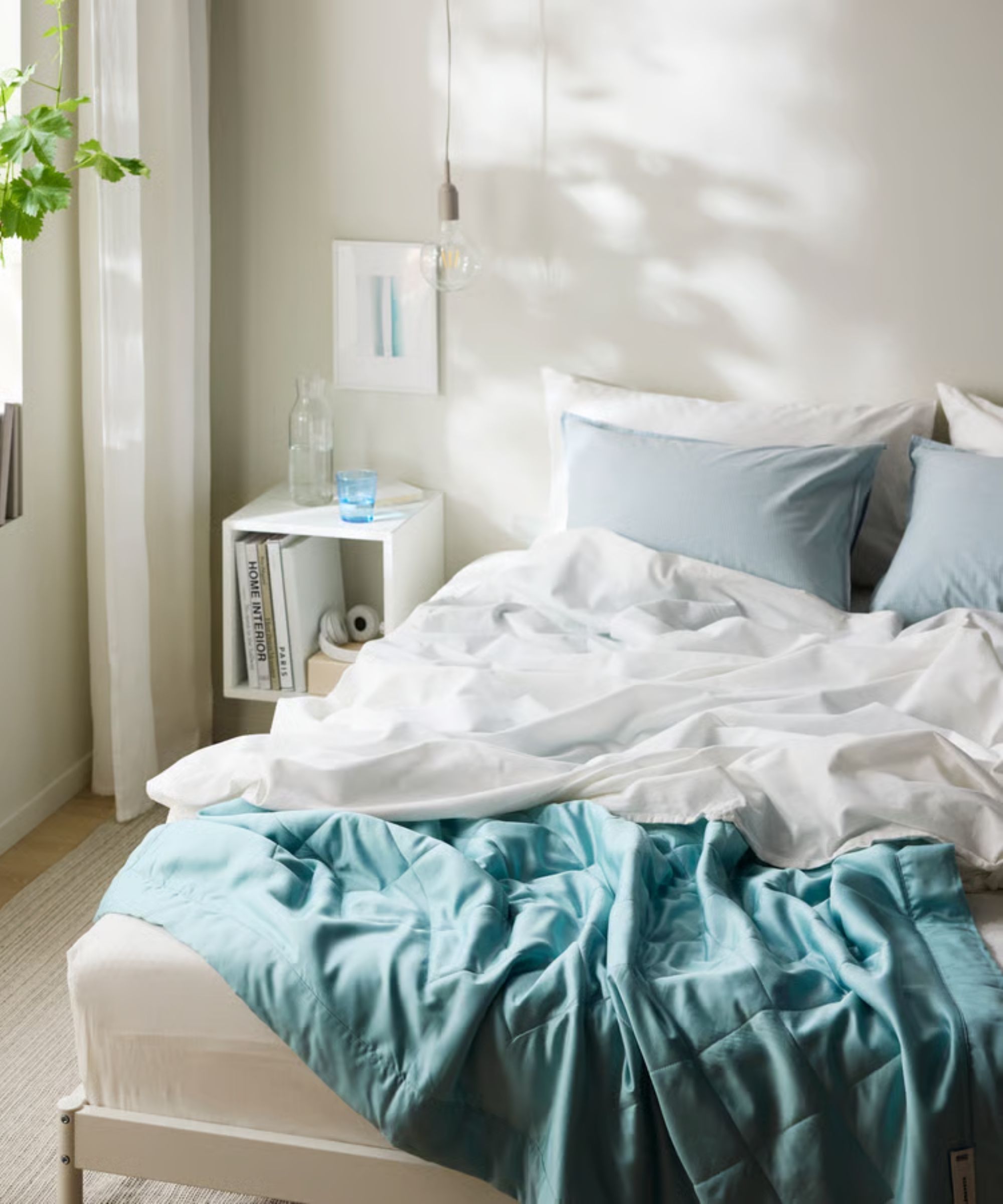 IKEA BL&amp;Aring;NEPETA Duvet insert on a white unmade bed in a white bedroom with white nightstand and houseplant.