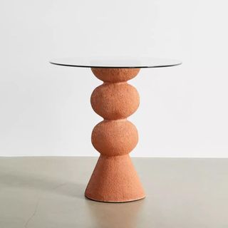 A glass-topped round dining table with a concrete globular base