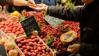 Two hands exchanging coins above a fruit market stall