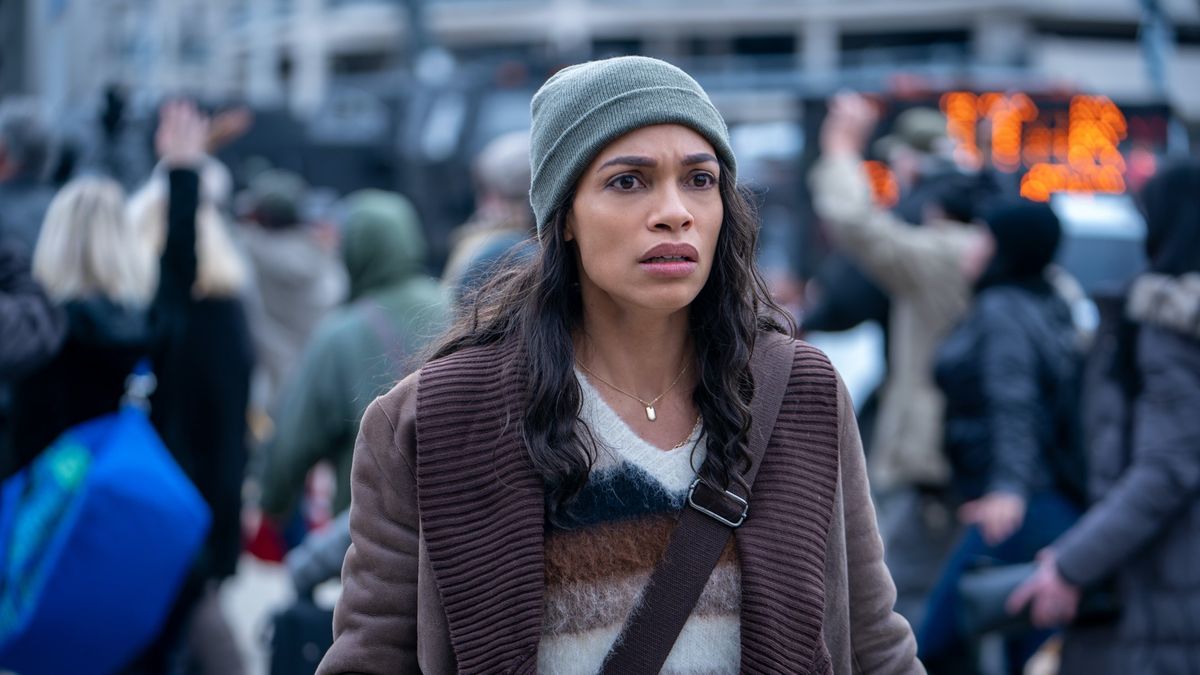 Rosario Dawson wearing a knit cap in a mass of people in DMZ