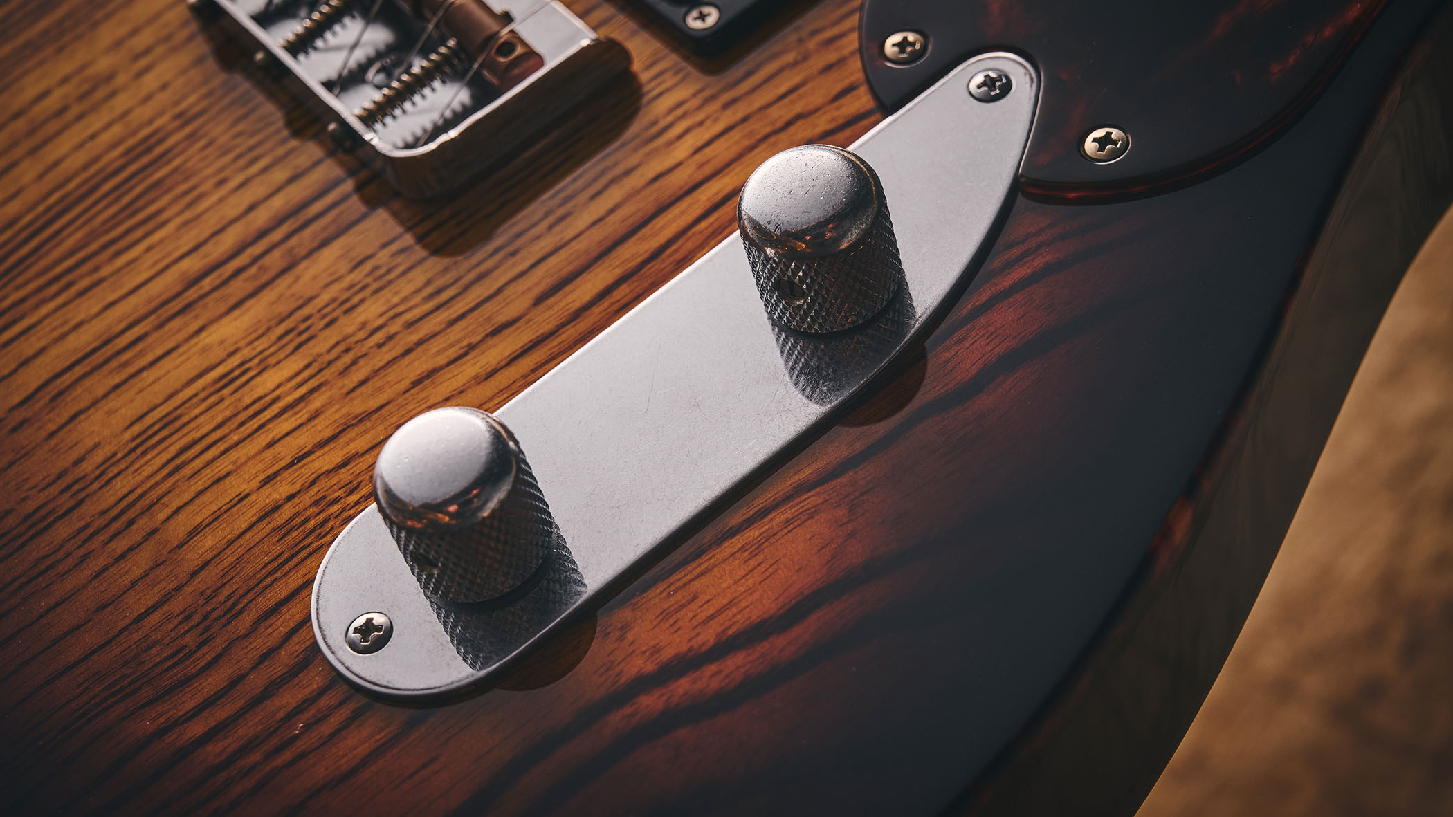 Patrick James Eggle Oz-t Cabronita Thinline; this semi-hollow T-style has a dark sunburst that reveals all the open grain, complementing the tortoiseshell pickguard, and is photographed here against a distressed floor, white and wooden backgrounds.