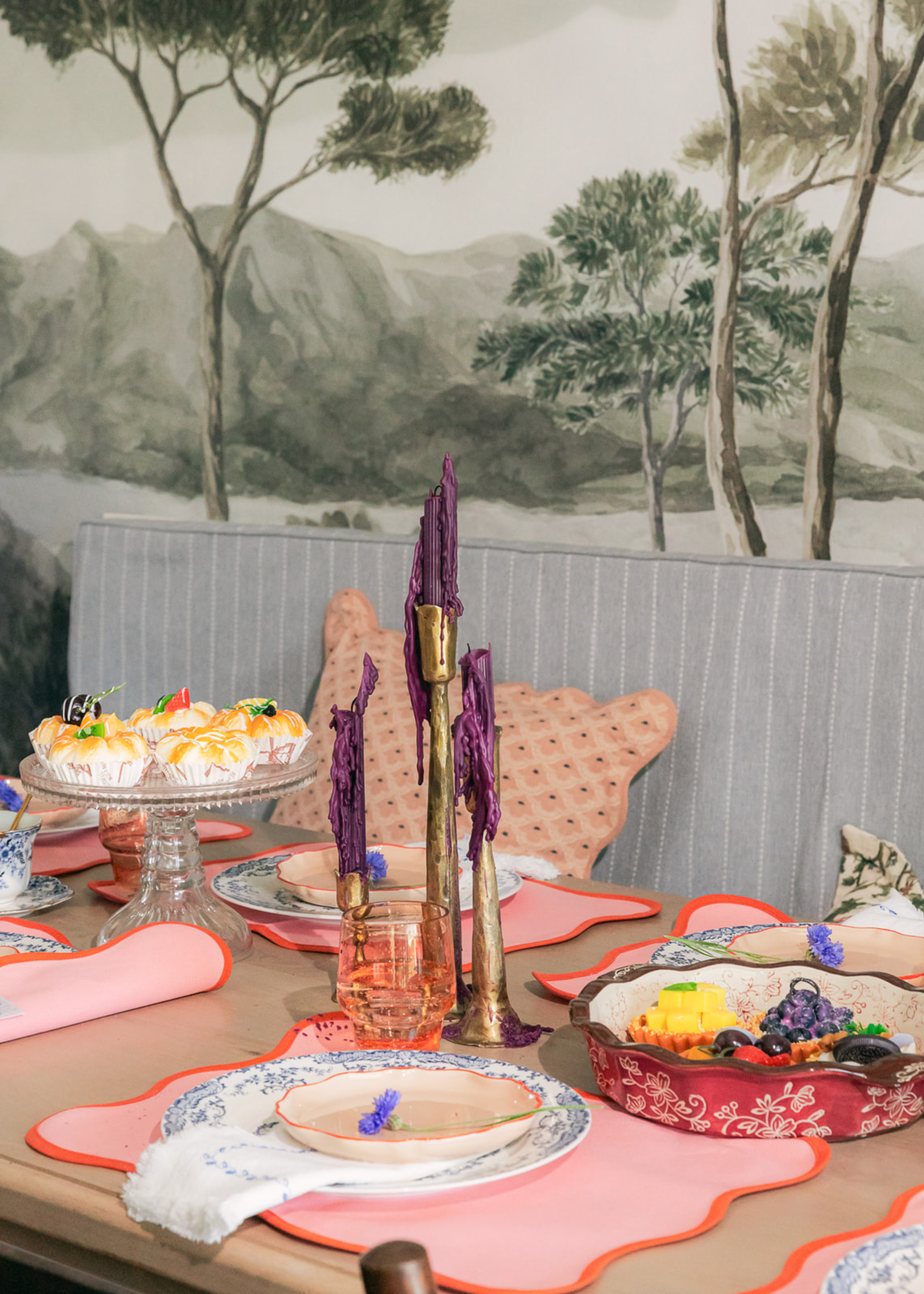A dining room with a dining table set with placemats, plates, a trio of candlesticks with melted purple candles and bowls of food