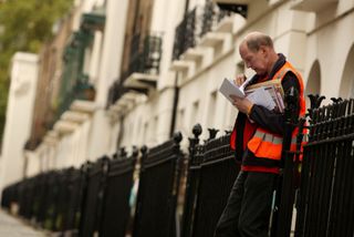a male royal mail postman looking and sorting through letters next to a wall