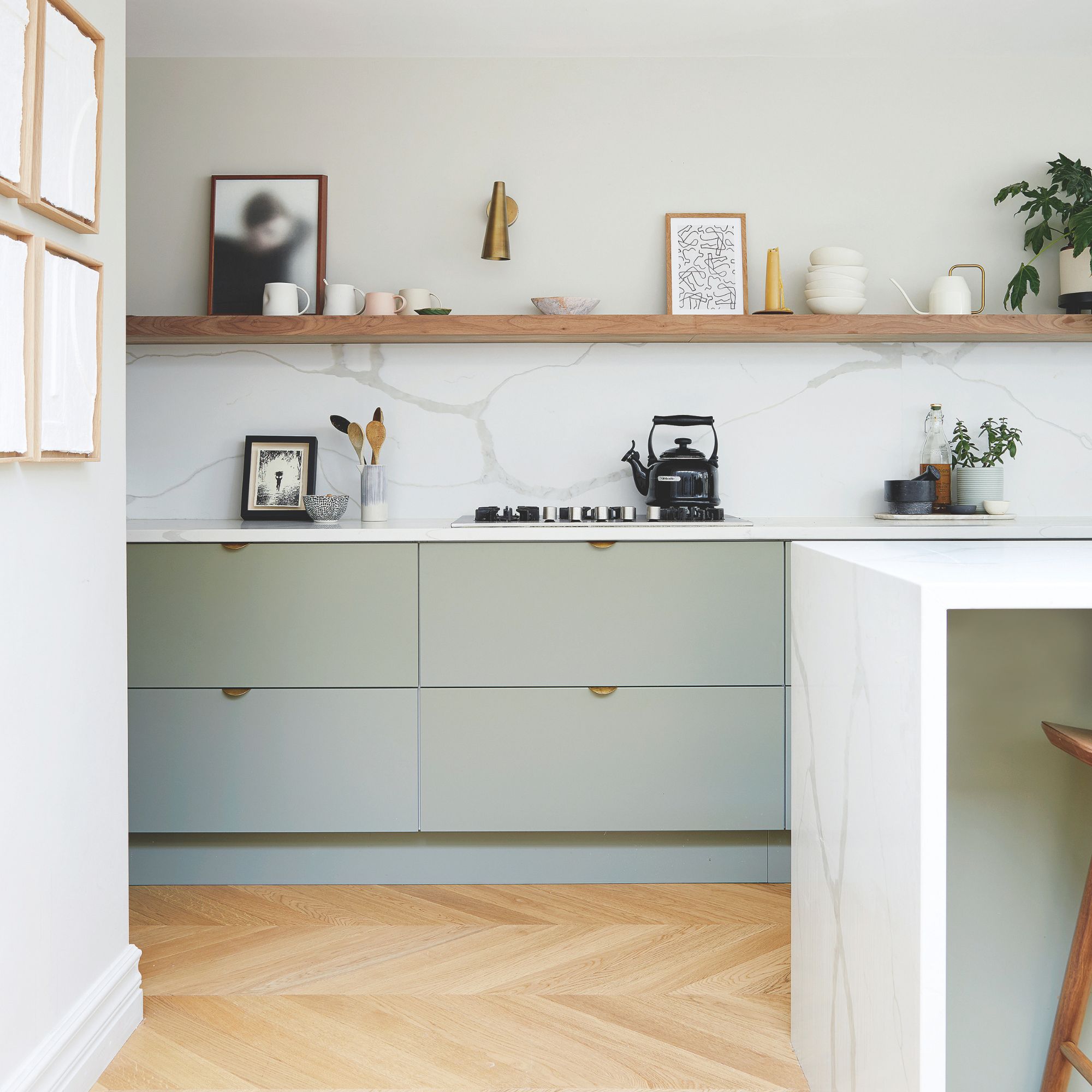 White painted kitchen with a marble splashback and sage green kitchen cabinets, with wooden flooring