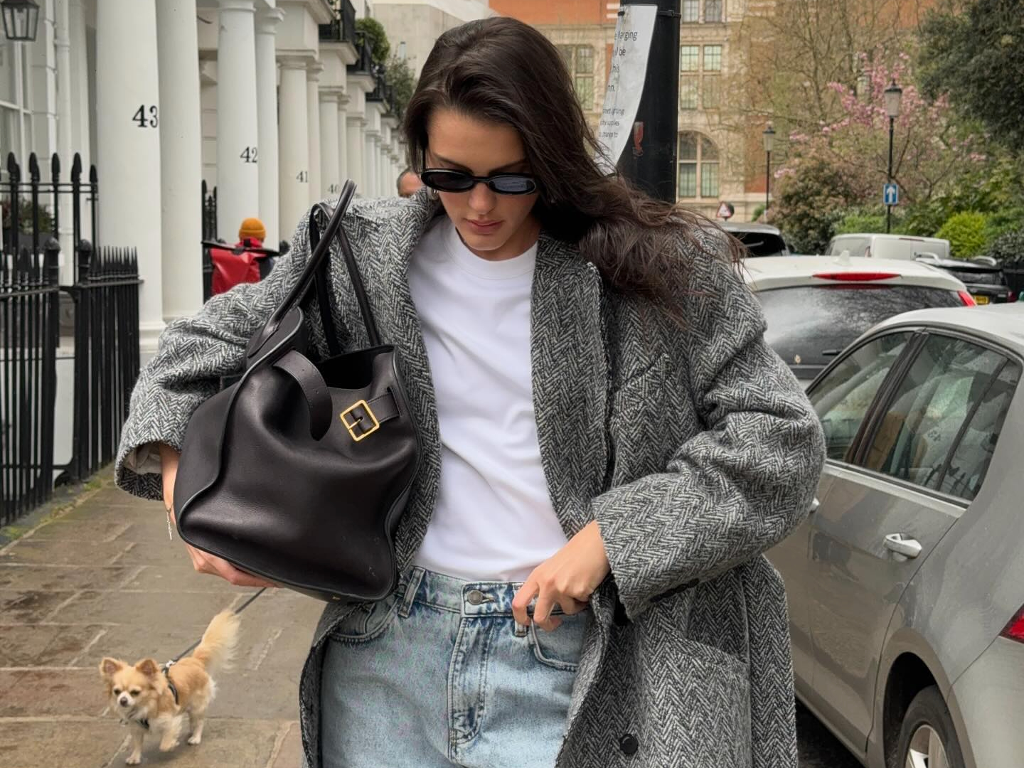 Fashion influencer Valeria in London wearing a chic fall outfit with faded baggy jeans, a white tee, long herringbone wool coat, and The Row's Margaux 17 black tote bag.