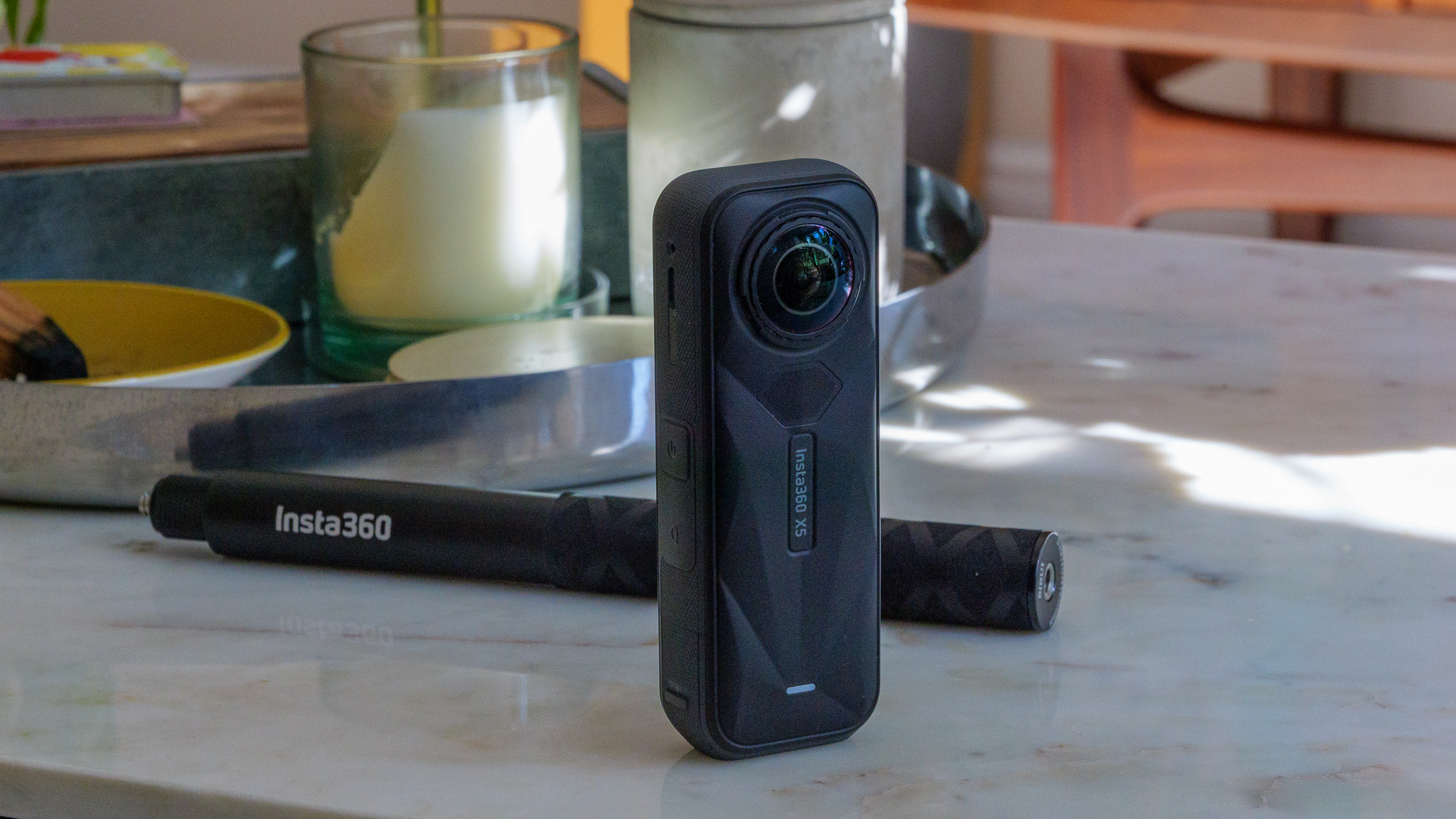 Insta360 X5 and selfie stick on a marble table in a sunlit room