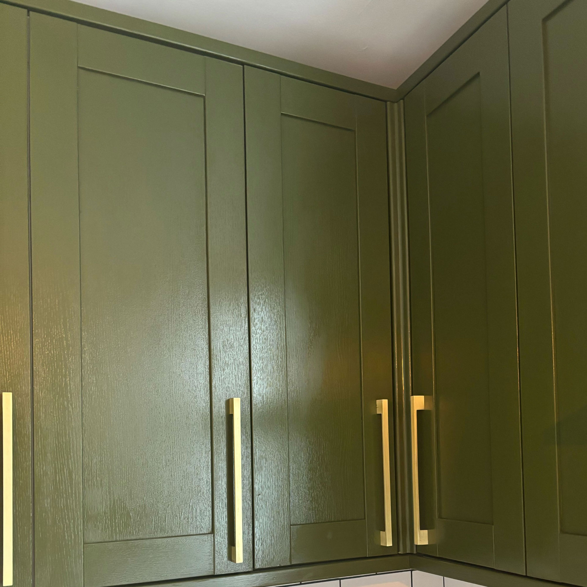 Green painted kitchen with gold handles and white countertops