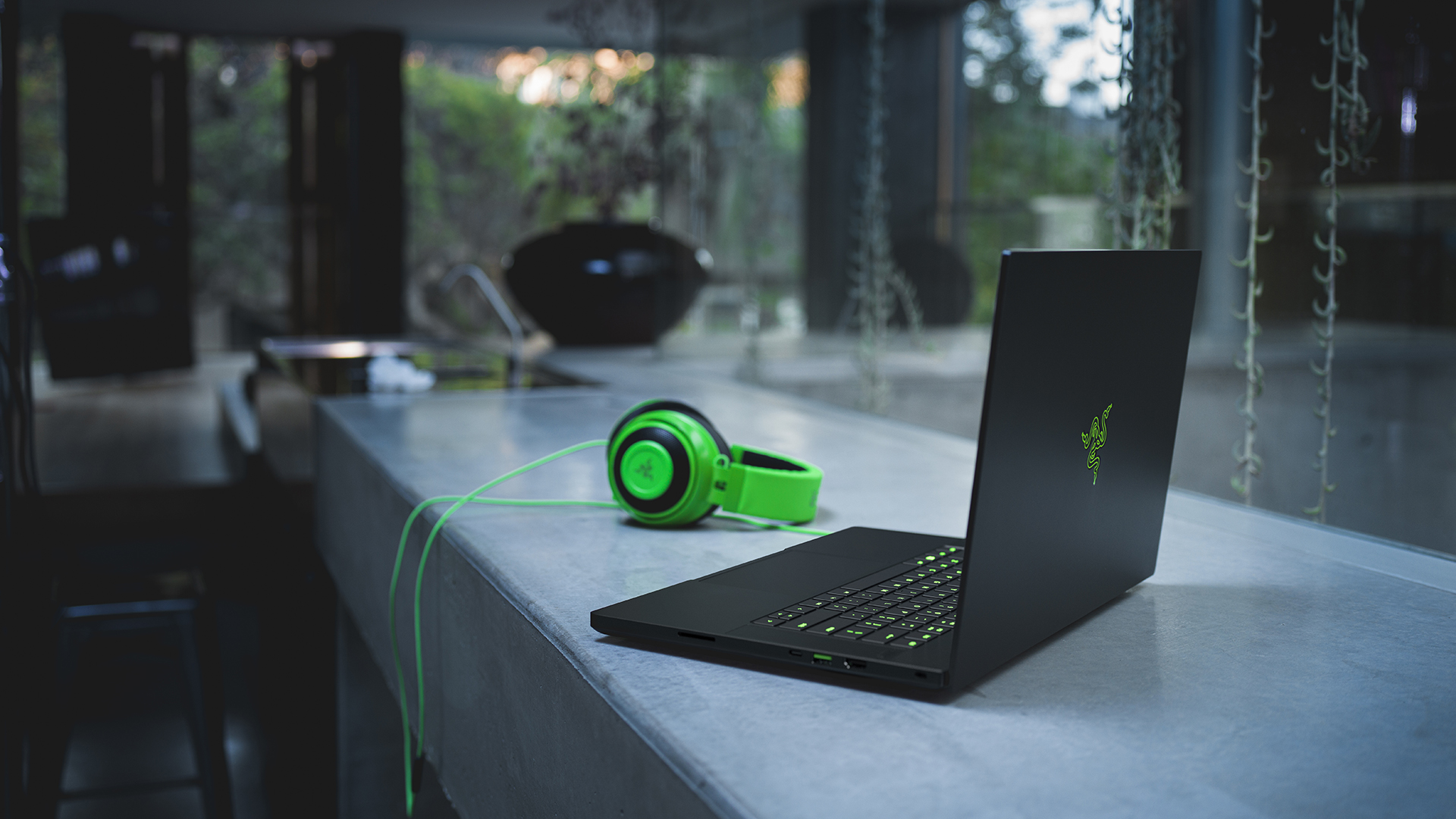 En Razer Blade 15 står öppnad på en vit bänk med ett par matchande Razer-hörlurar bredvid.