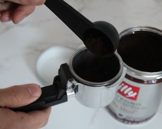 Camryn Rabideau using measuring scoop to measure Illy ground espresso into Mr. Coffee espresso maker portafilter