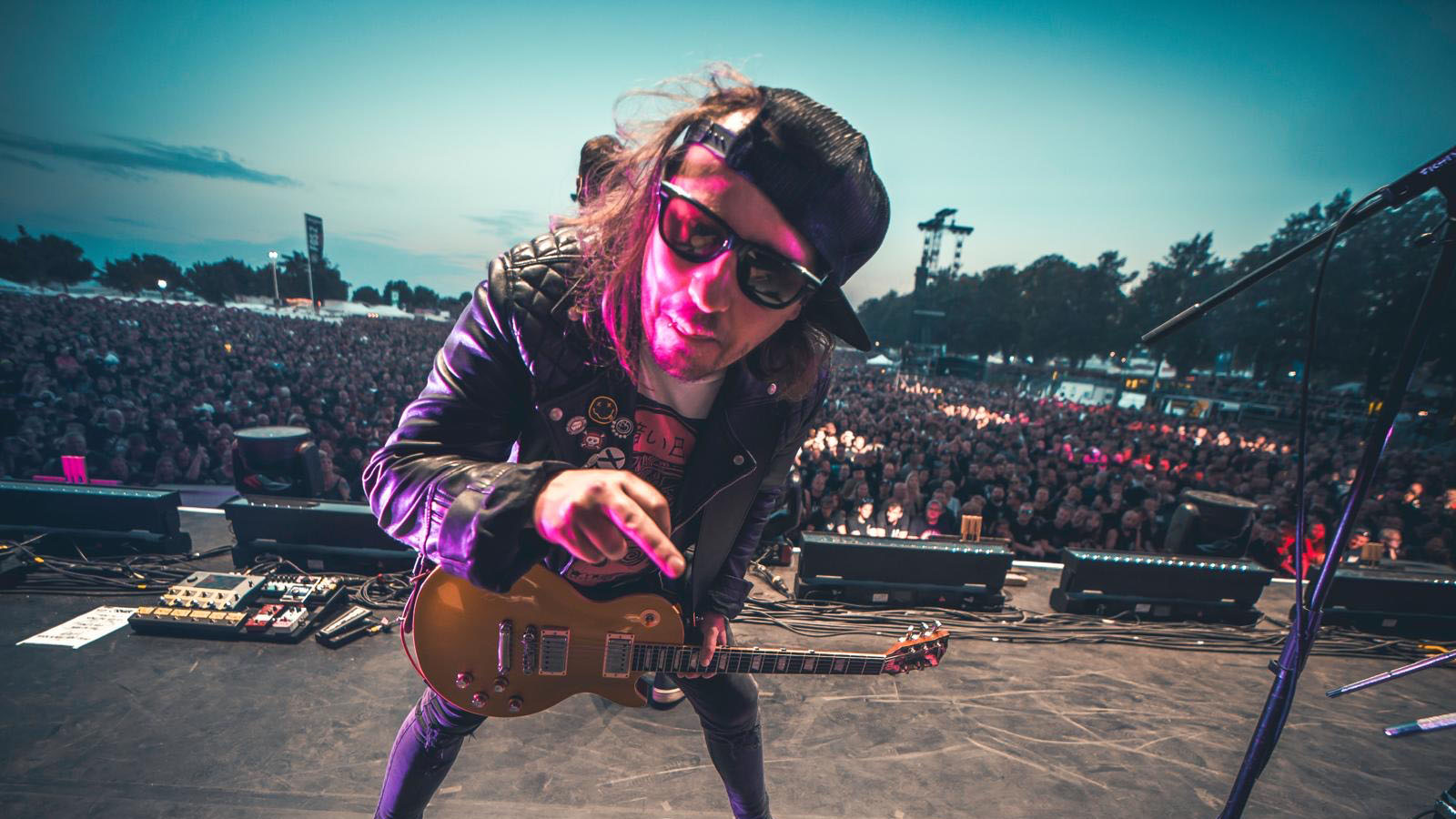 Ian &quot;Shiner&quot; Thomas of Those Damn Crows onstage playing to a festival crowd with his Gibson Les Paul. He wears a baseball cap and sunglasses.