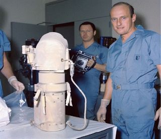The Surveyor 3 camera shown with astronaut Pete Conrad and technicians at the NASA Lunar Receiving Laboratory upon its receipt after the Apollo 12 mission Nov. 1969. The camera was then bagged for later studies, including the microbial sampling of the camera.