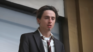 Timothee Chalamet in a suit on the edge of a window during an SNL sketch.